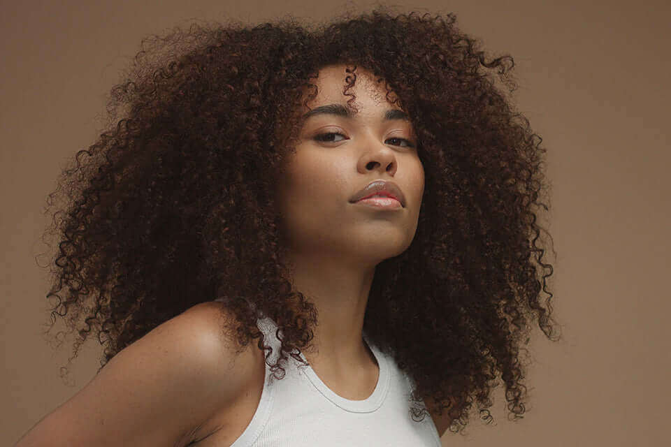 Femme aux cheveux afro volumineux, montrant une belle texture crépue et éclatante sur fond neutre.