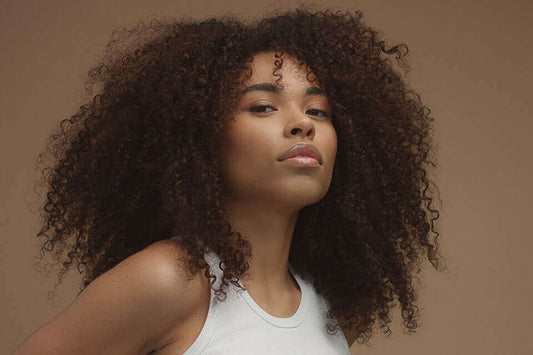 Femme aux cheveux afro volumineux, montrant une belle texture crépue et éclatante sur fond neutre.