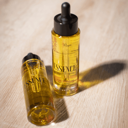 Bouteilles d'huile de pousse ESSENCE – Nuée By Milie pour cheveux crépus et bouclés, sur surface en bois.